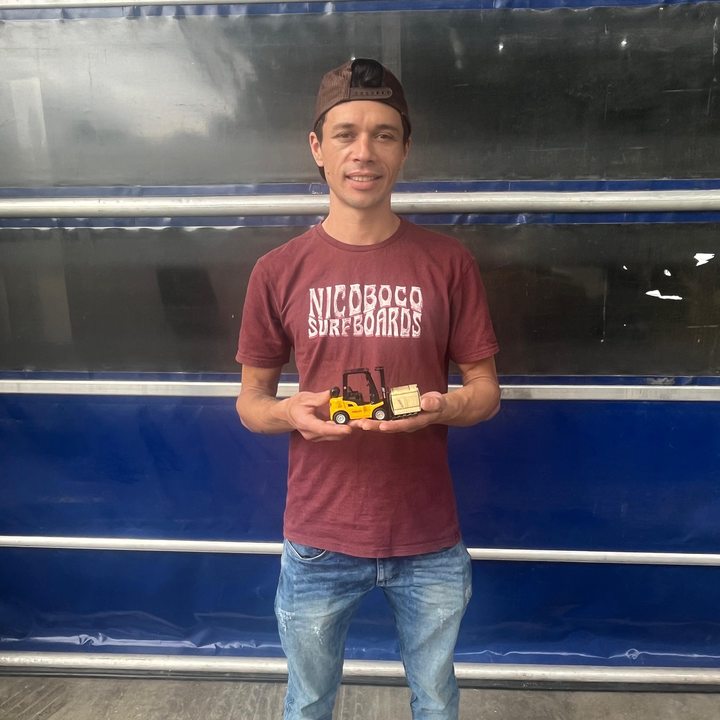 Colaborador com miniatura de empilhadeira em portão industrial